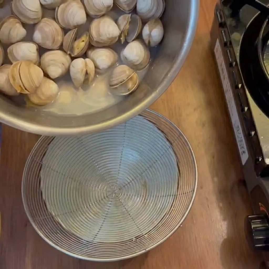 Die aromatische Brühe wird aus den gekochten Muscheln in eine darunter stehende Schüssel abgeseiht.