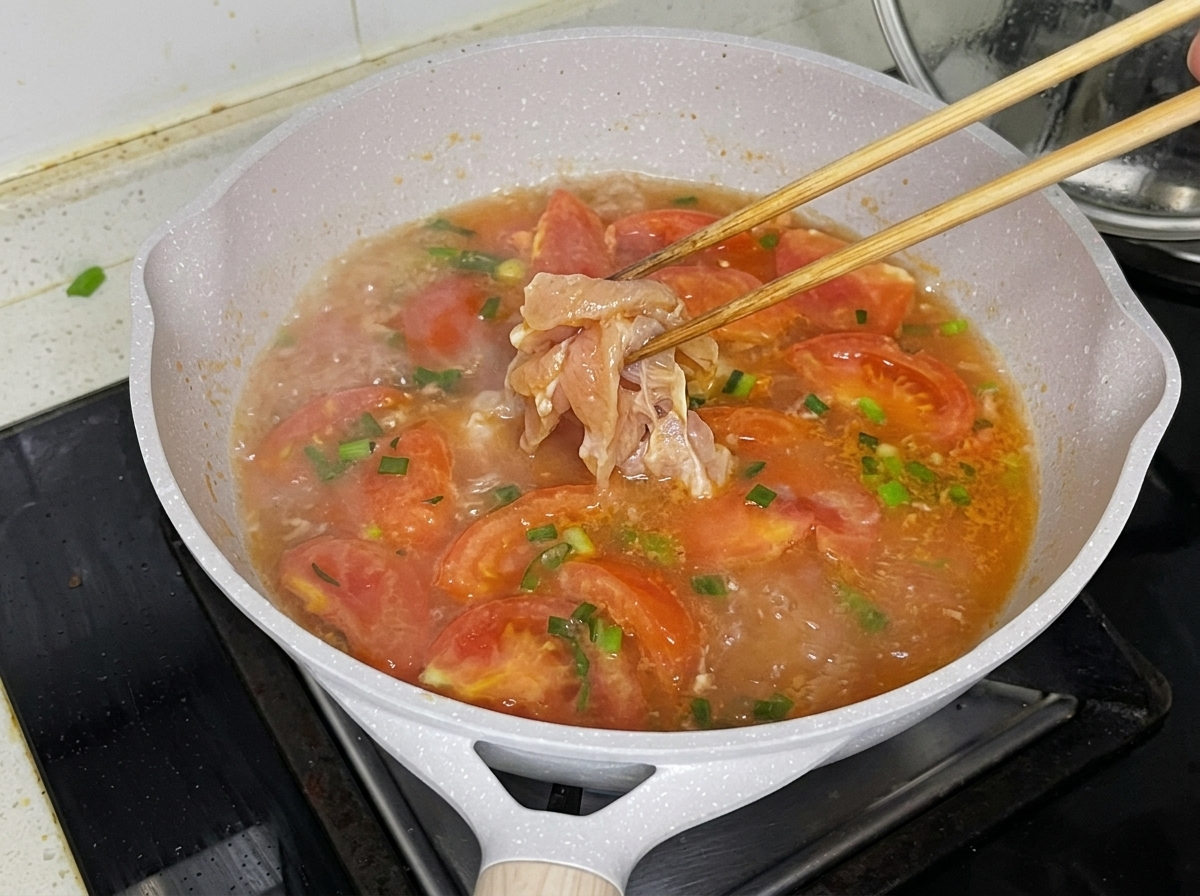 Hähnchenbruststücke werden vorsichtig mit Stäbchen in die köchelnde Tomatenbrühe gegeben.