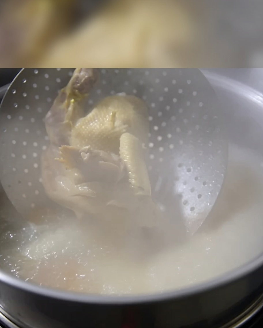 Ein ganzes gekochtes Huhn wird in einen Topf mit siedender Knochenbrühe gegeben.