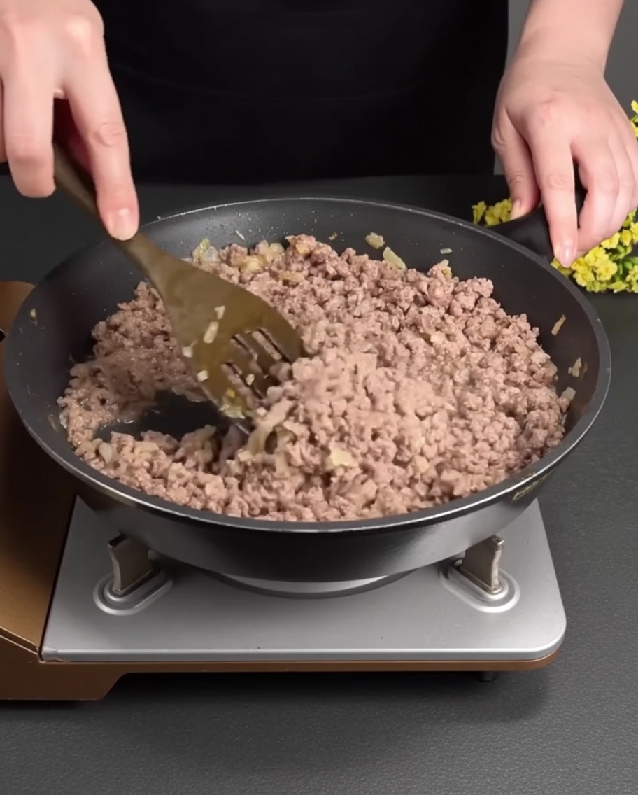 Rinderhackfleisch brät in einer Pfanne zusammen mit dem weichen Gemüse.