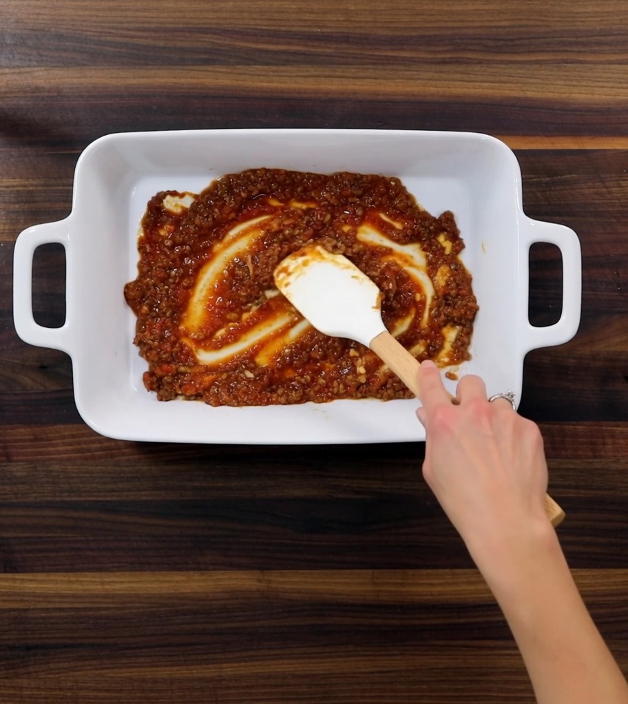Eine Auflaufform wird mit Fleischsauce, Nudelplatten und weißer Sauce geschichtet.
