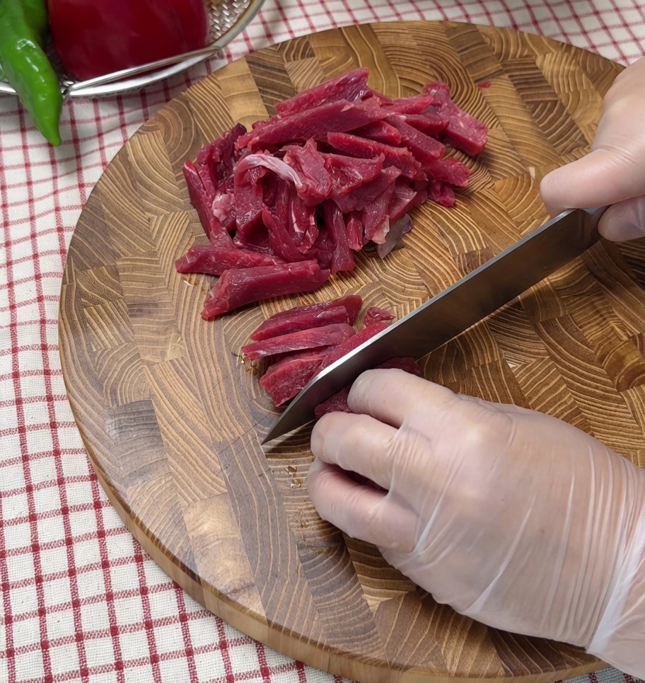Rohes Rindfleisch wird auf einem Holzbrett in dünne Streifen geschnitten.