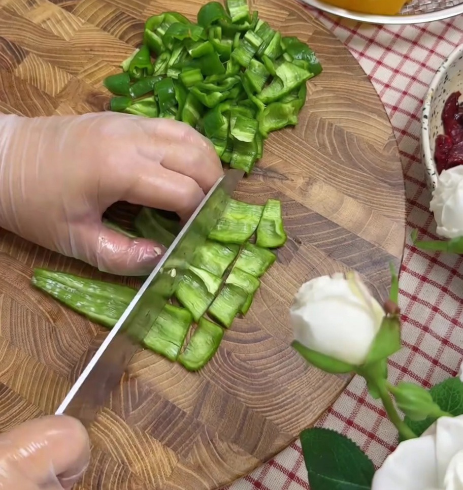 Paprika und rote Zwiebel werden auf einem Schneidebrett in kleine Stücke gehackt.