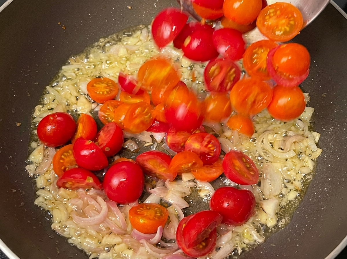 Angebratene Zutaten und Tomaten schmoren zusammen in der Pfanne.