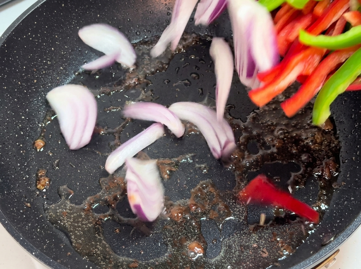 Zwiebel- und Paprikastreifen werden in einer heißen Pfanne angebraten.