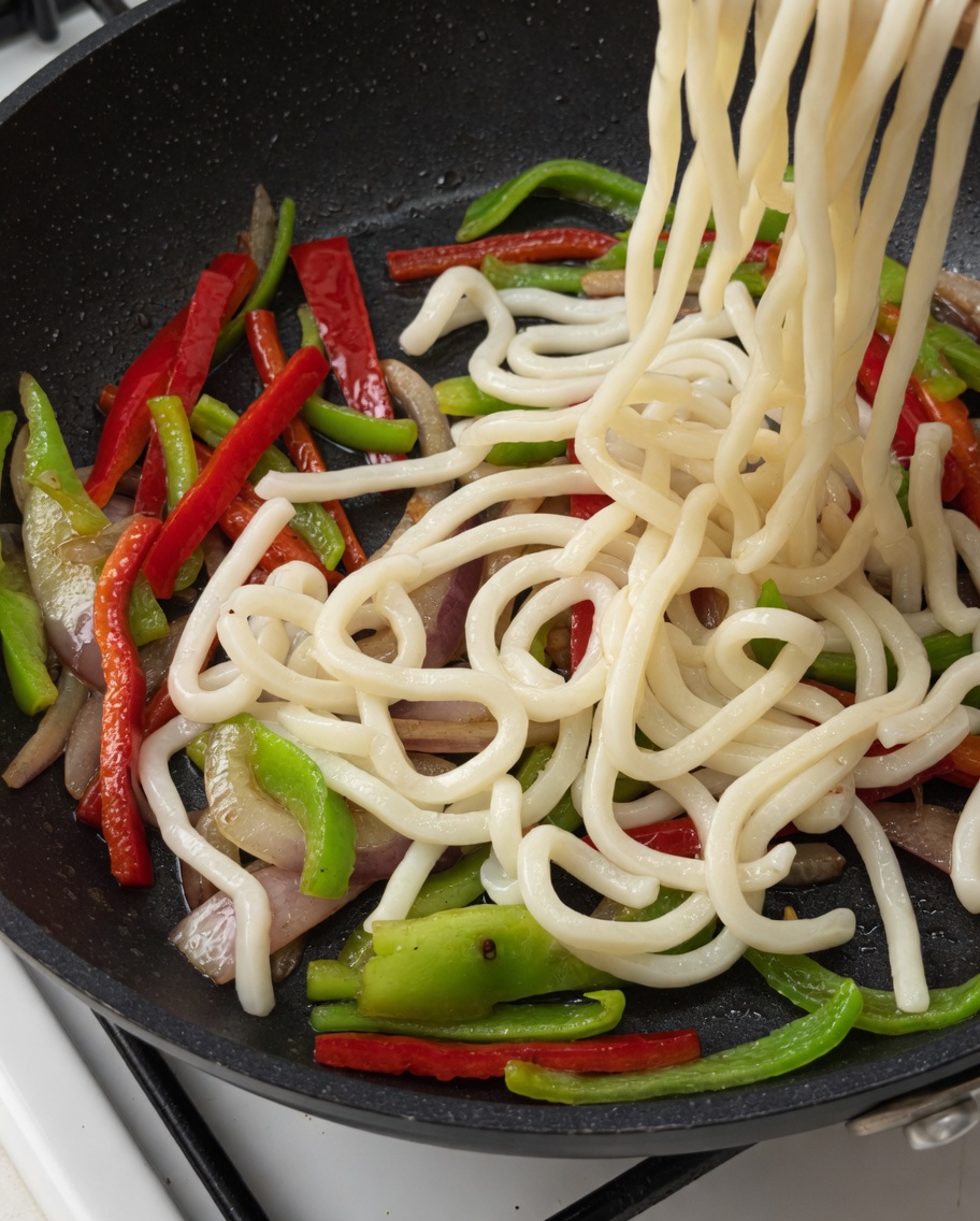 Udon-Nudeln und gebratenes Rindfleisch werden in die Pfanne zum Gemüse gegeben.
