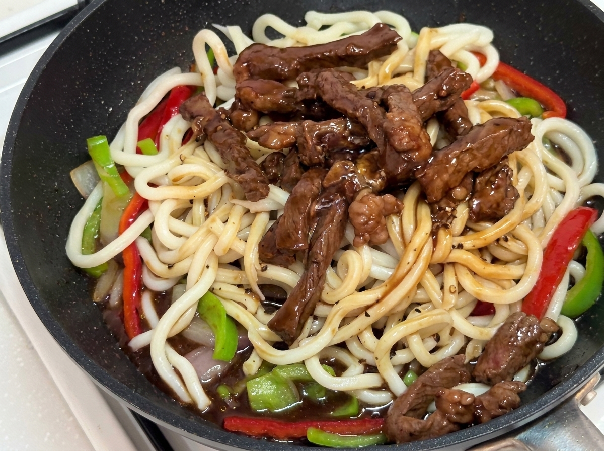 Das Gericht wird in der Pfanne mit einer Zange durchgeschwenkt, bis alles mit Sauce überzogen ist.