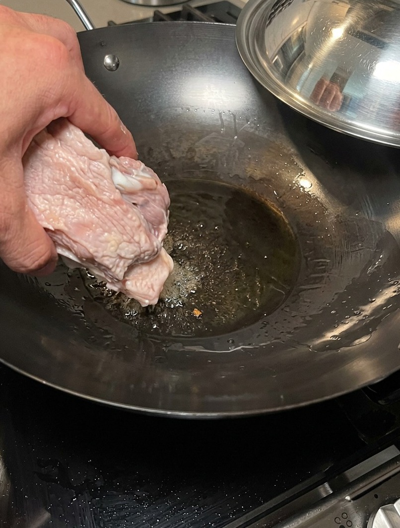 Schweineknochen werden in einem heißen Wok angebraten, um eine geröstete Geschmacksgrundlage zu entwickeln.