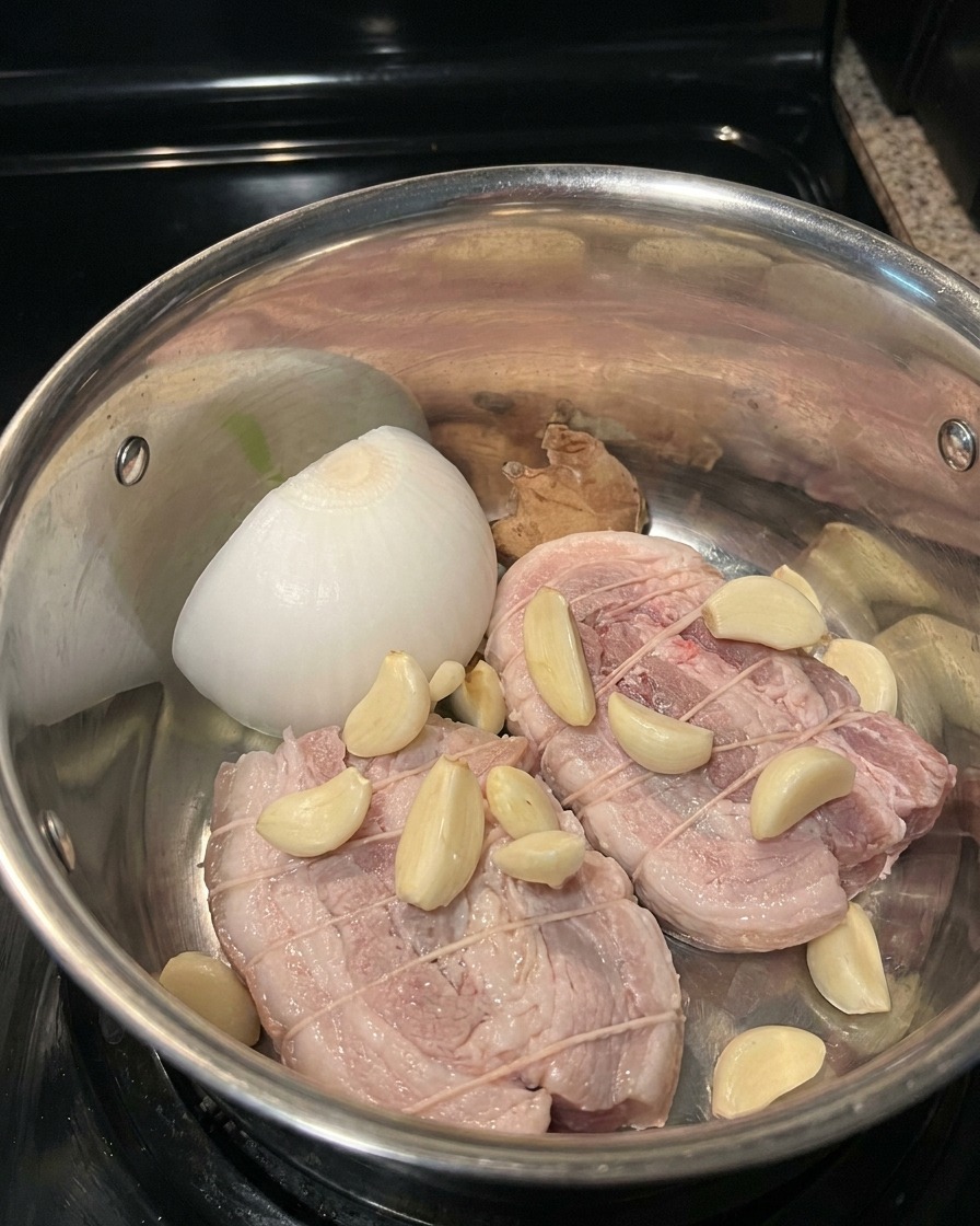Schweinebauchstücke mit Aromen und Schmorsud in einem Edelstahltopf.