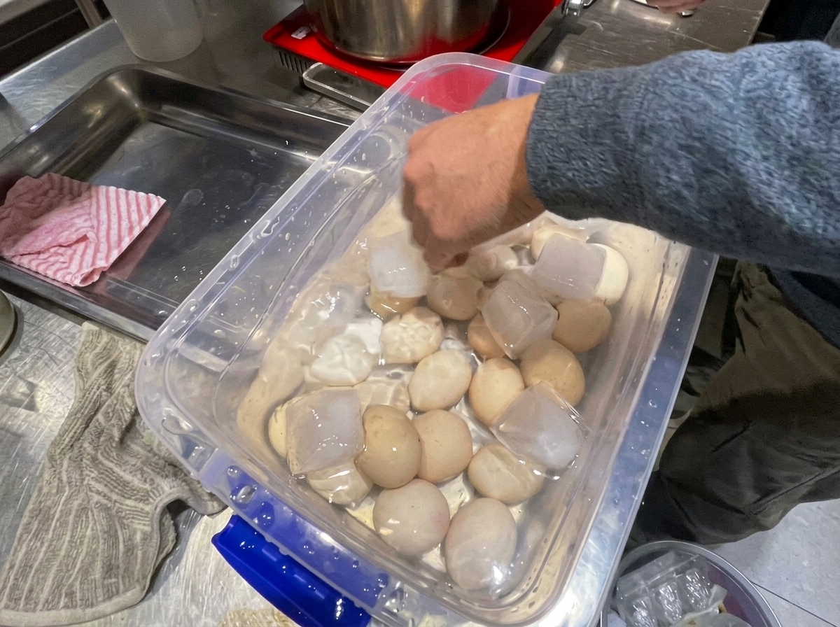 Ein gekochtes Ei, das vorsichtig mit einem Löffel in einer Schüssel mit kaltem Wasser geschält wird.