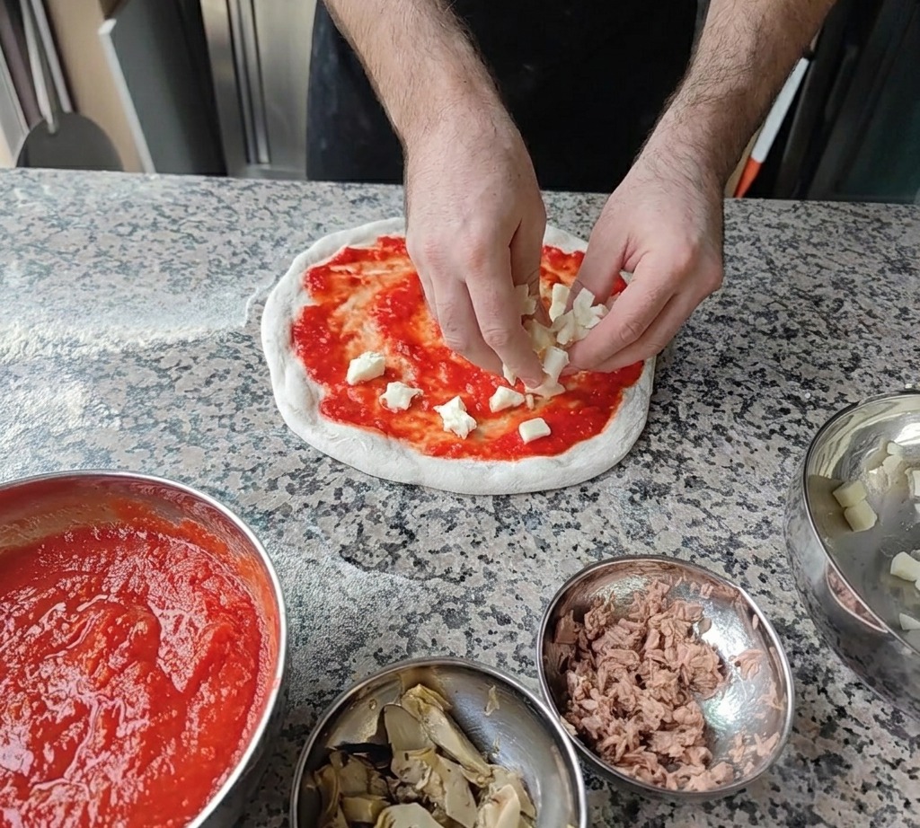 Kleine Würfel aus frischem weißem Mozzarella werden auf der Tomatensauce verteilt.