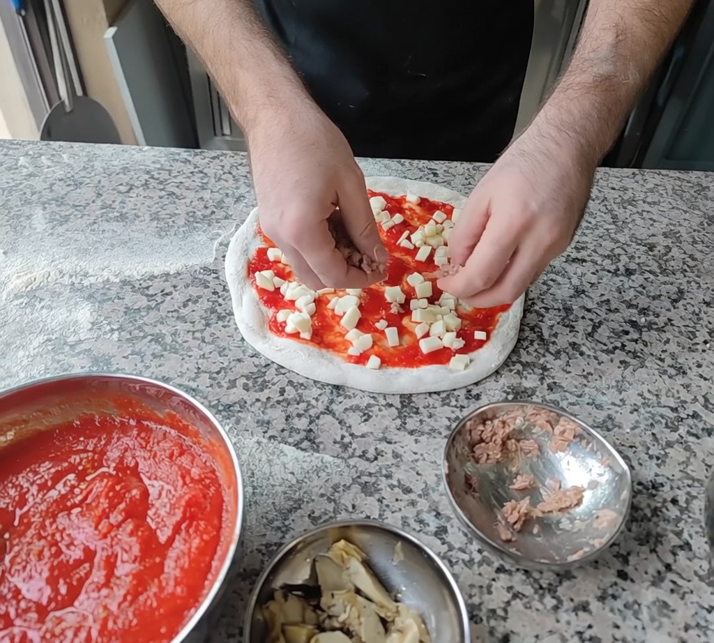 Thunfischflocken und Artischockenscheiben werden als letzte Zutat auf die Pizza gelegt.
