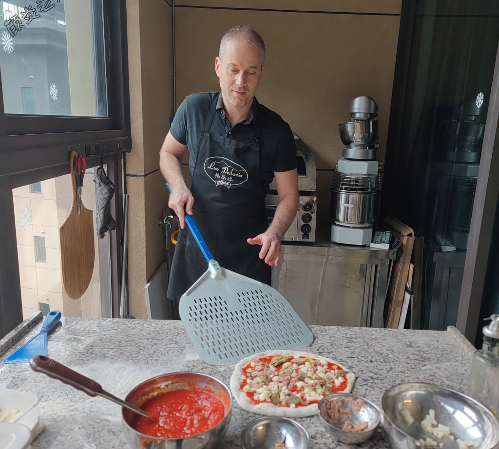 Ein metallener Pizzaschieber wird unter die vorbereitete Pizza geschoben.