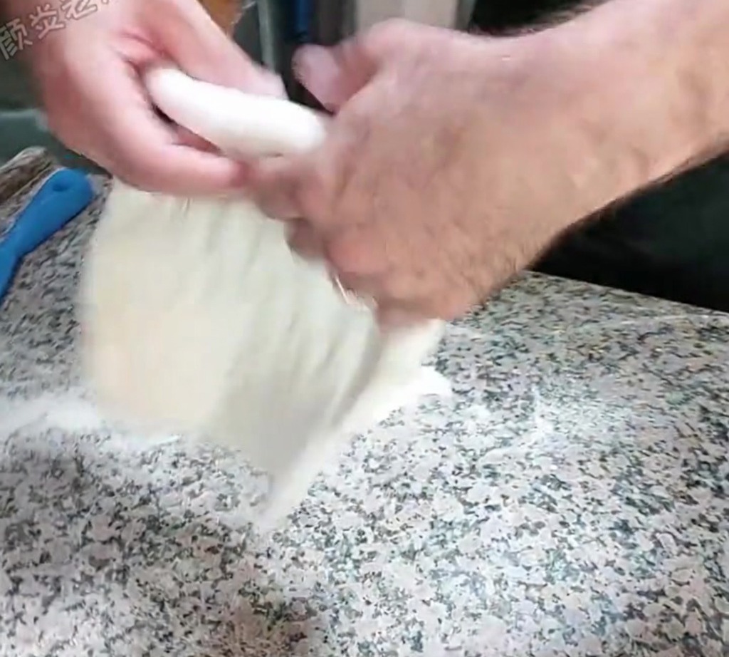 Der Teig wird mit einer Klopfbewegung auf einer bemehlten Arbeitsplatte von Hand gedehnt.