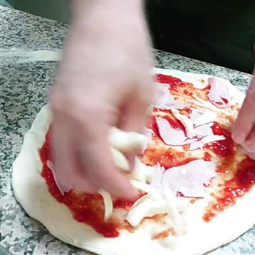 Stücke von Mozzarella werden auf den Pizzaboden gegeben.