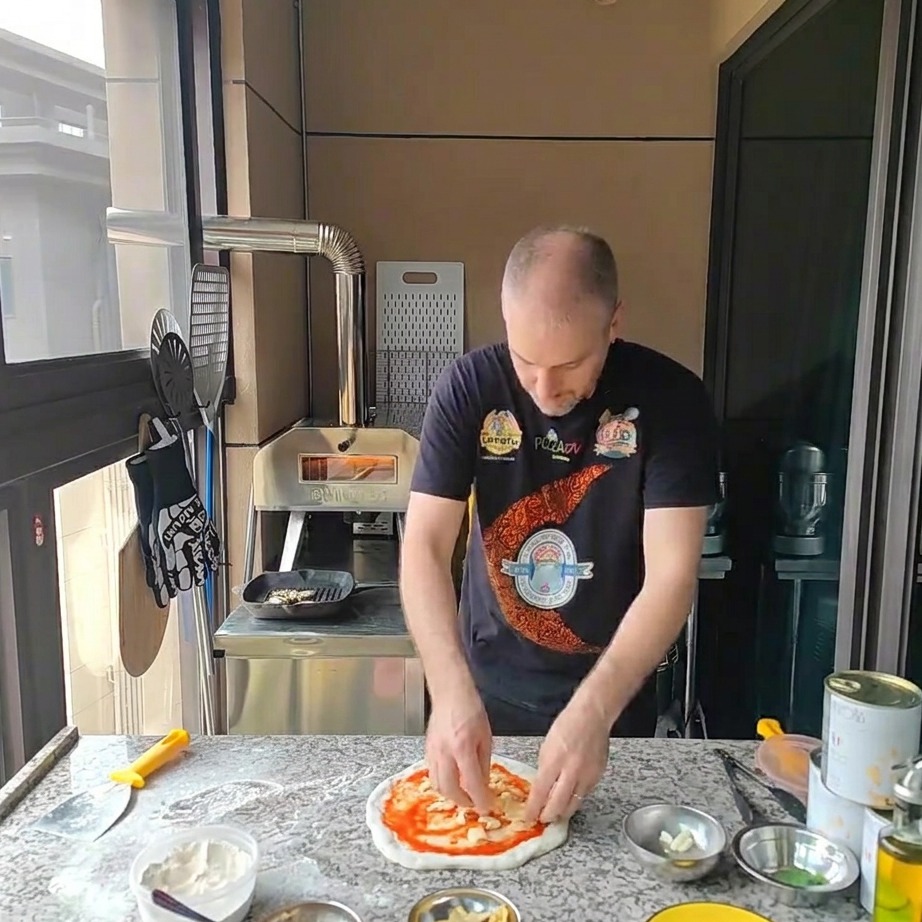 Geriebener Mozzarella wird auf der Pizza verteilt.