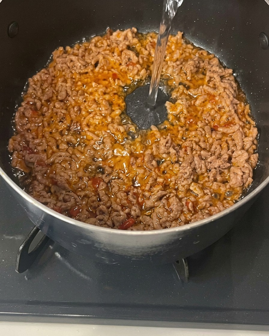 Wasser wird in den Topf zum angebratenen Fleisch gegossen.