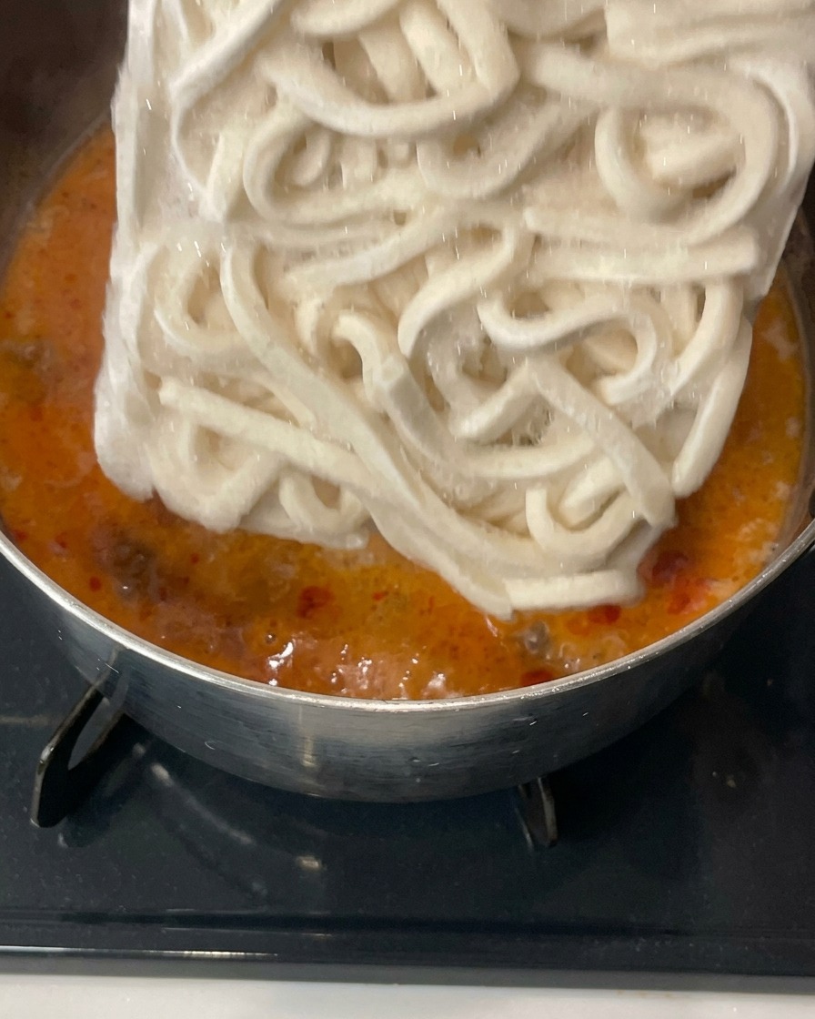 Ein Block tiefgekühlte Udon-Nudeln wird in die köchelnde Suppe mit Sojasprossen gegeben.