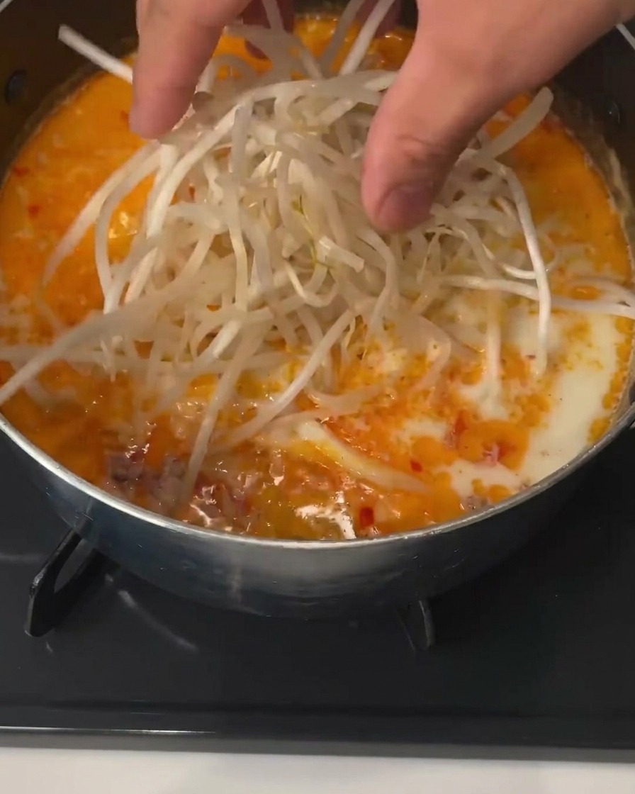 Sojasprossen werden in der orangefarbenen Miso-Brühe untergetaucht.