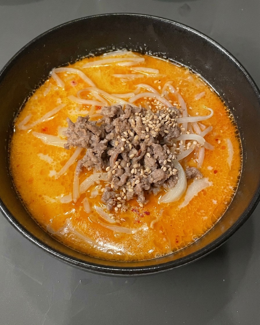 Nahaufnahme einer Schüssel Tantan Udon, garniert mit weißem Sesam und gehackten Frühlingszwiebeln.
