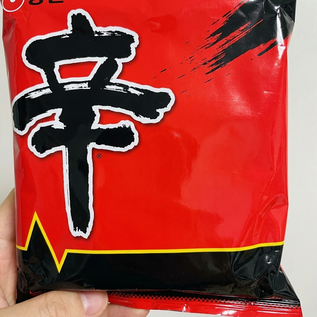Rotes Würzpulver aus einer Shin Ramyun-Packung wird zum gebratenen Hackfleisch in den Topf gegeben.