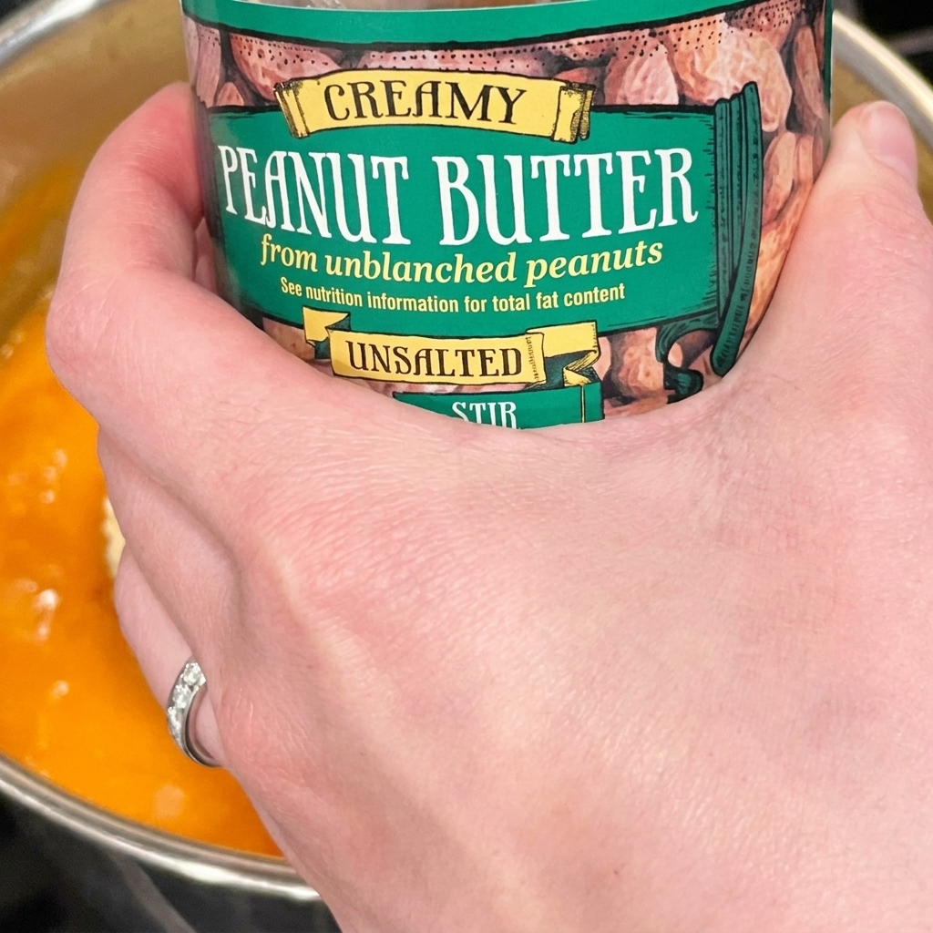 Ein großer Löffel cremige Erdnussbutter wird in die sprudelnde Nudelbrühe gerührt.