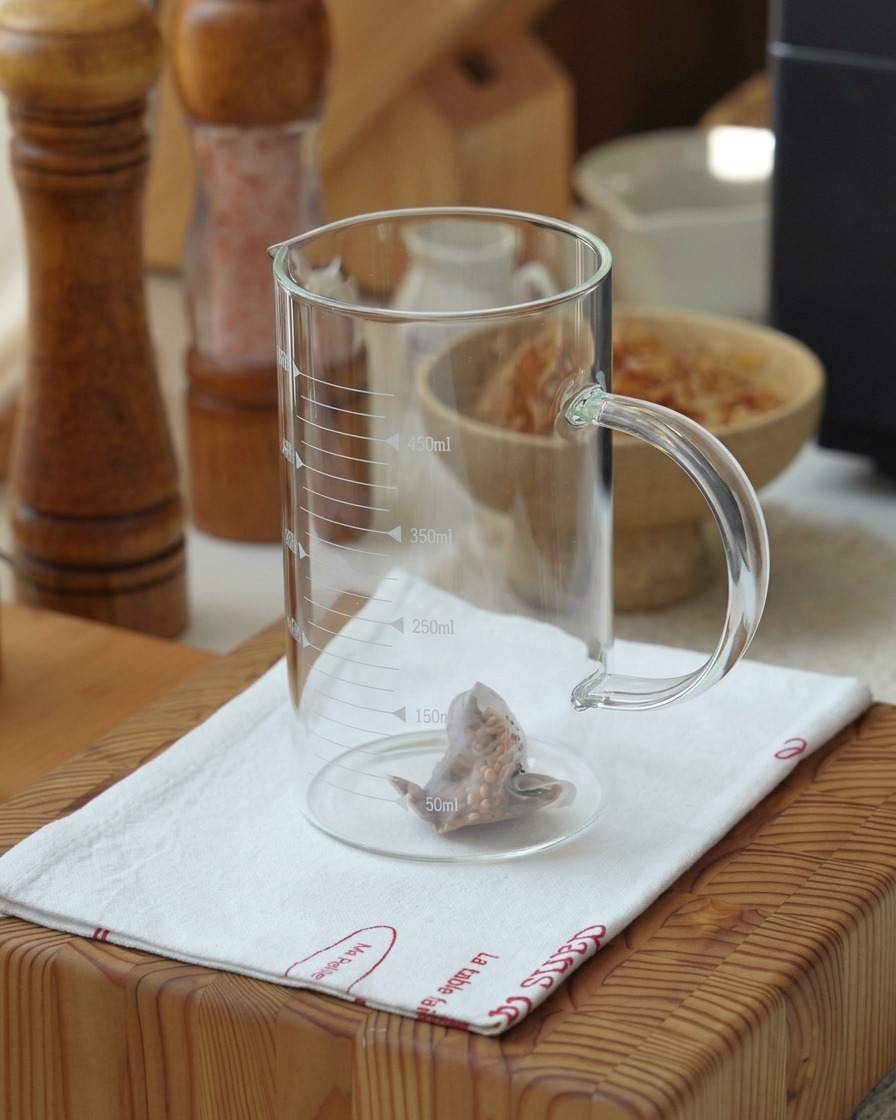 Ein Genmaicha-Teebeutel zieht in heißem Wasser in einem Messbecher.