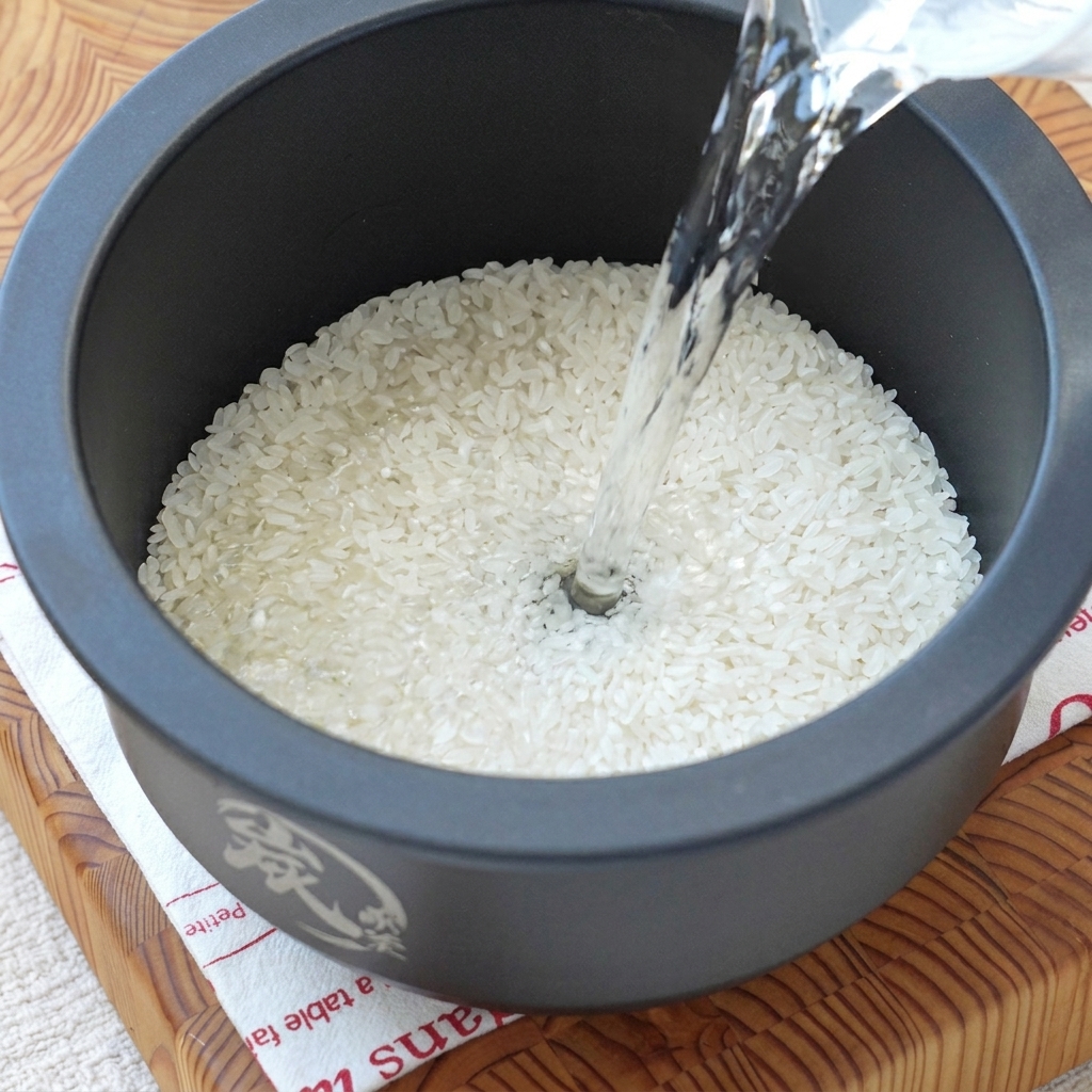 Wasser wird in den Topf eines Reiskochers zu rohem Reis gegeben.