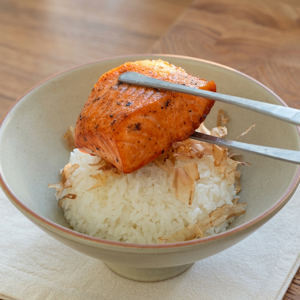 Ein gebratenes Lachsfilet wird mit einer Zange auf den Reis gesetzt.