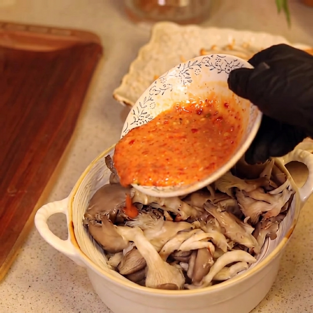 Eine Hand mit schwarzem Handschuh gießt Sauce über eine Schüssel mit Pilzen.