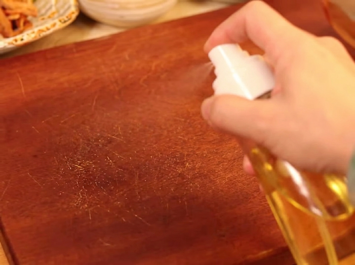 Eine Hand sprüht mit einer Sprühflasche leicht Öl auf Pilze, die auf einem Backblech angerichtet sind.