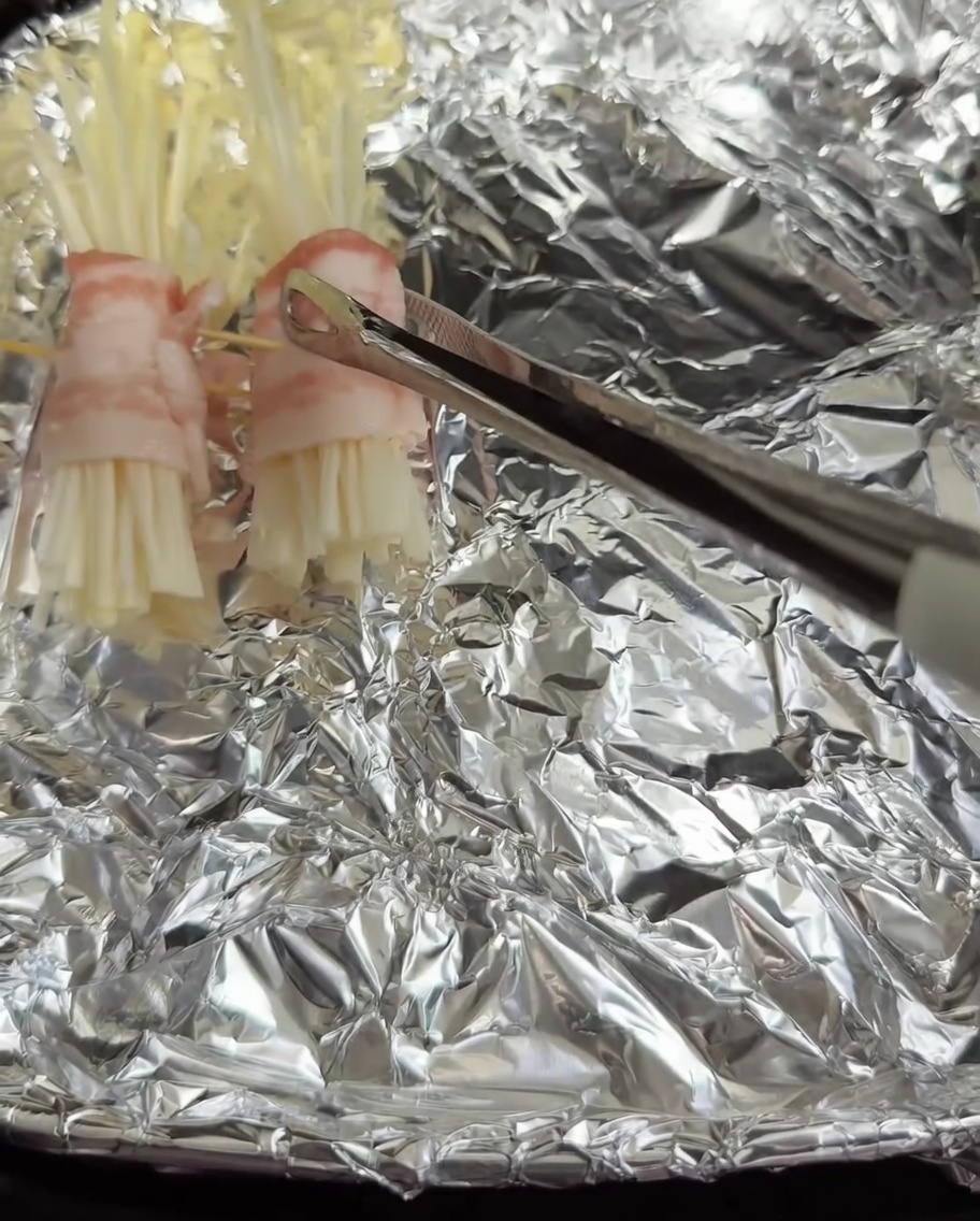 Zusammengesetzte Schweinebauch-Enoki-Röllchen werden in einen mit Alufolie ausgelegten Air-Fryer-Korb gelegt.
