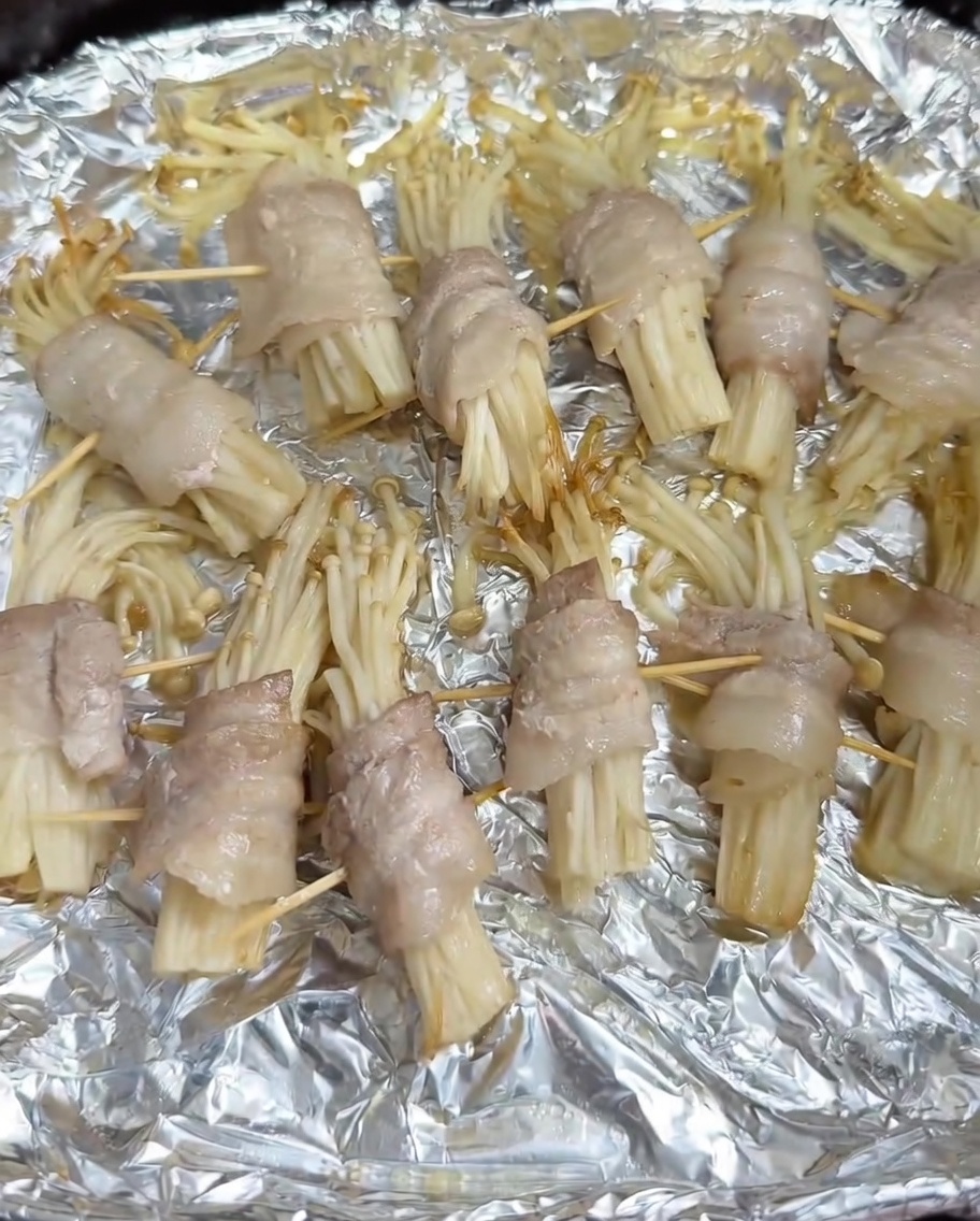 Barbecue-Gewürz wird auf die halbgegarten, in Schweinebauch eingewickelten Enoki-Röllchen im Air-Fryer-Korb gestreut.
