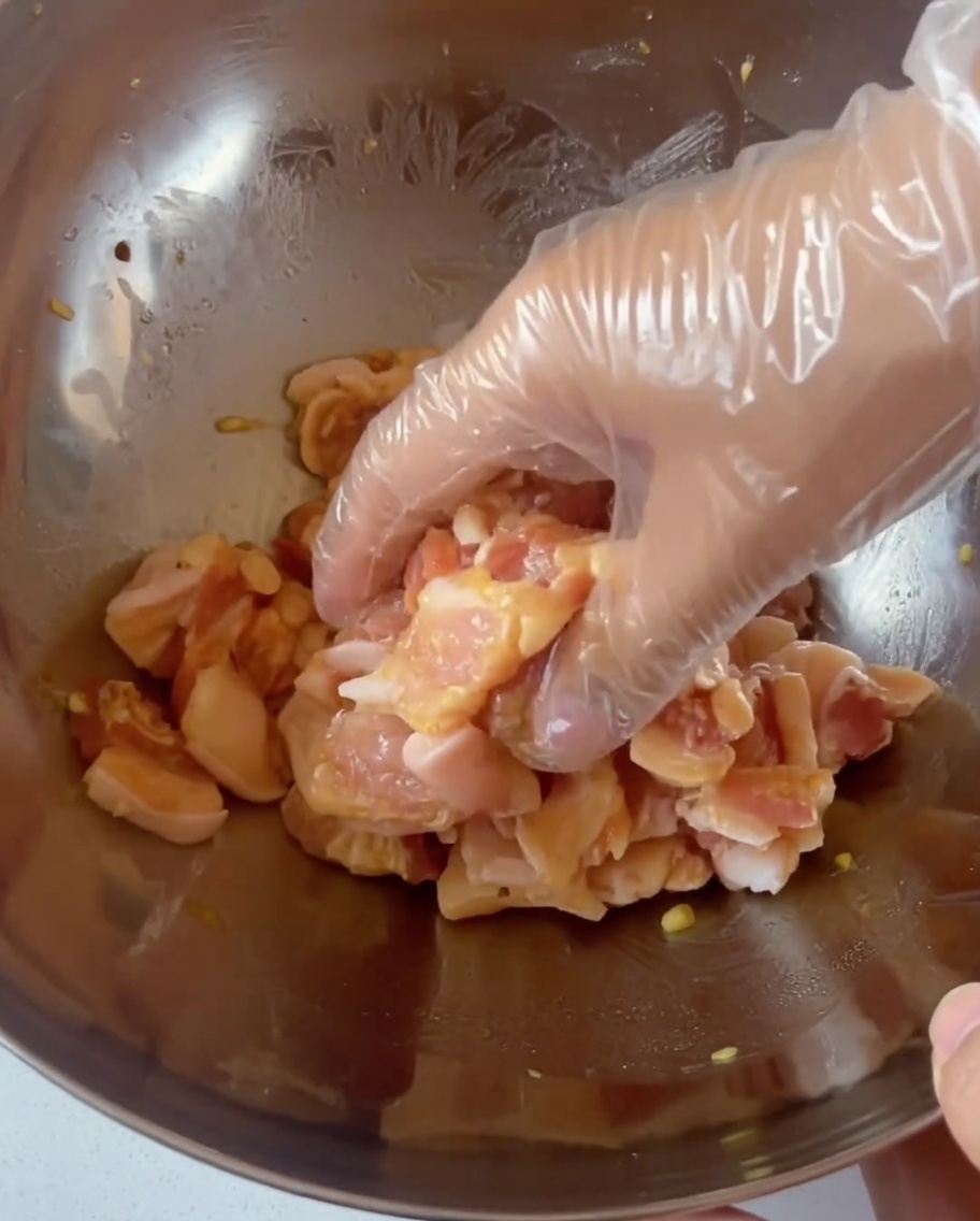 Eine behandschuhte Hand vermengt das marinierte Fleisch.