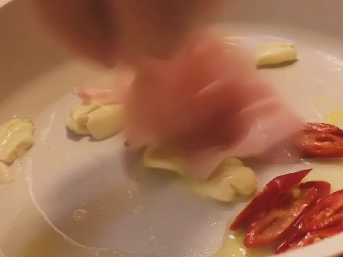 Schweinebauchstreifen brutzeln in einer hellen Pfanne zusammen mit Knoblauch und roten Chilis.