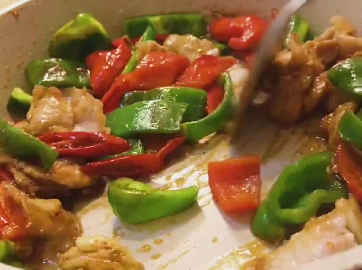 Eine bunte Mischung aus Schweinefleisch, grüner und roter Paprika wird in einer Pfanne mit einem Holzspatel geschwenkt.
