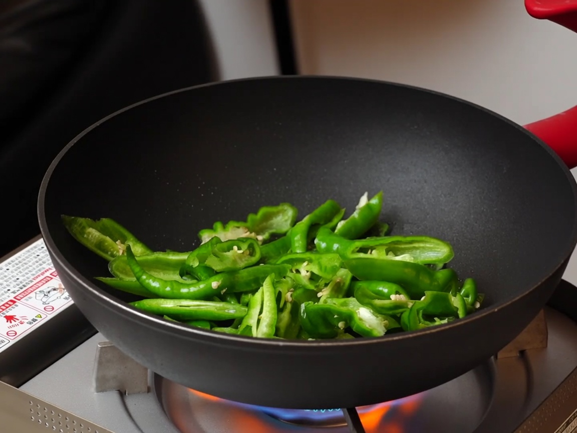 Geschnittene grüne Paprika werden in einer dunklen Antihaftpfanne über einem tragbaren Gaskocher angebraten.