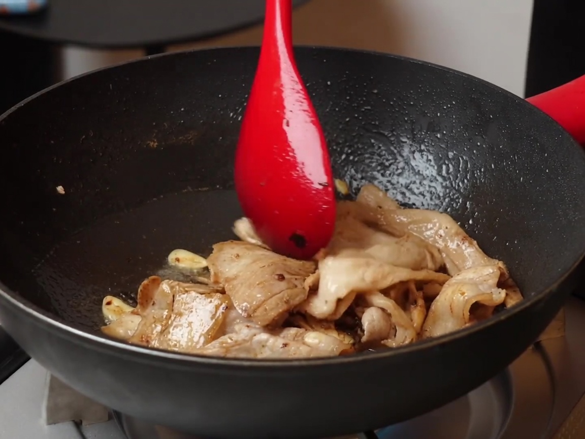 Eine Nahaufnahme von heller und dunkler Sojasauce, die über gebratenen Schweinebauch, Knoblauch und schwarze Bohnen in einer Antihaftpfanne gegeben wird.