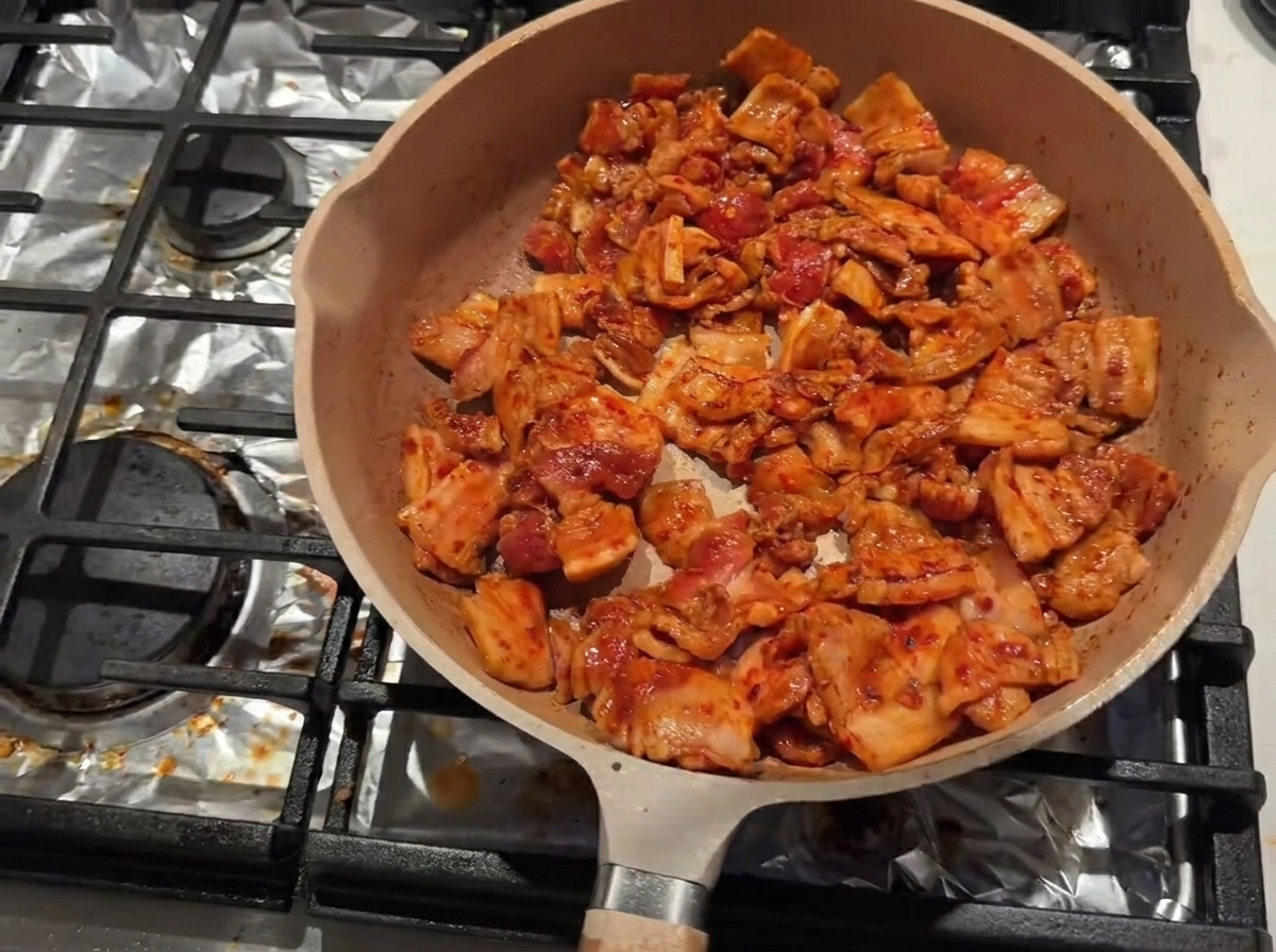 In der Pfanne brät der Schweinebauch, während Kochwein entlang des inneren Randes hinzugefügt wird.