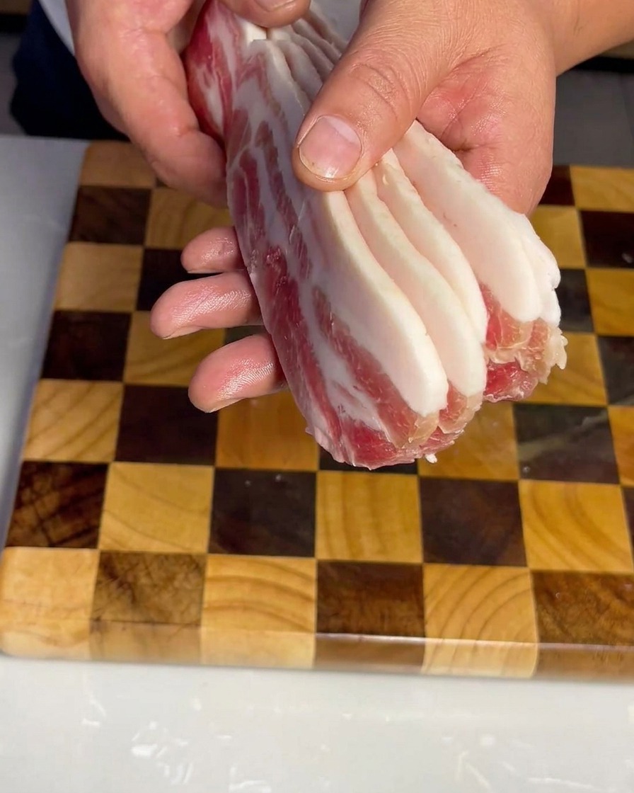 Gleichmäßige Streifen aus rohem Schweinebauch auf einem Holzschneidebrett.