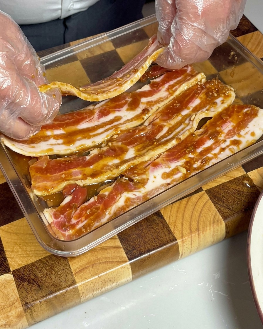 Marinierte Schweinebauchstreifen in einem Behälter, vollständig von brauner Miso-Sauce bedeckt.