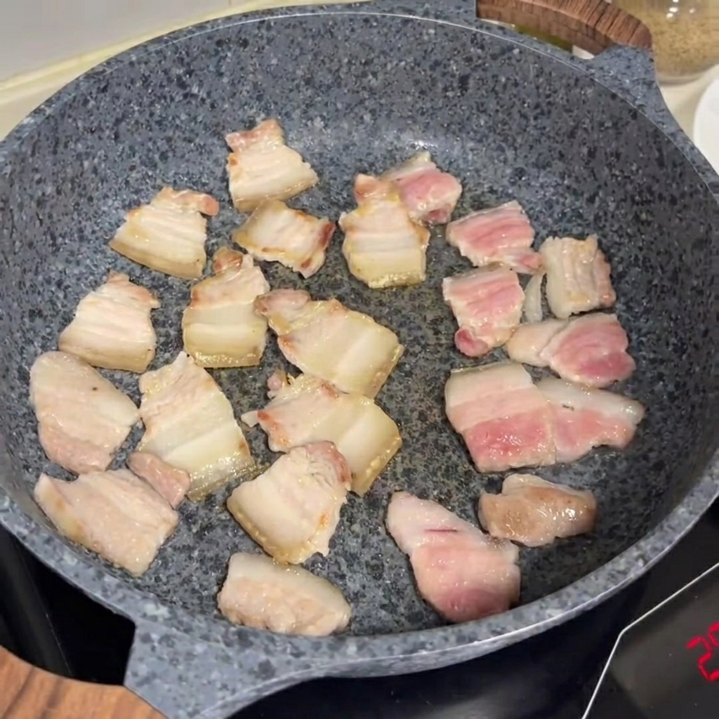 Schweinebauchscheiben bräunen in einer grauen Steinpfanne.