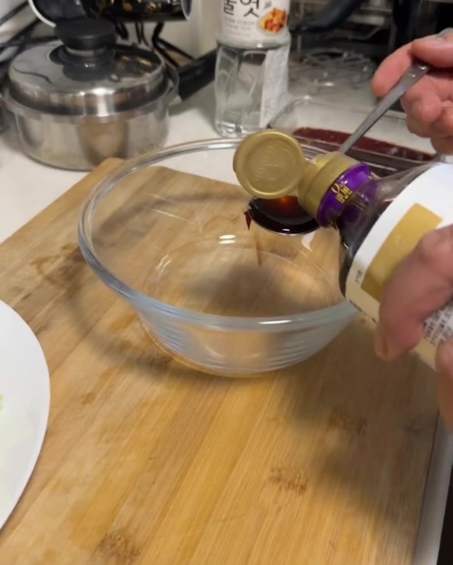 Hand gießt Sojasauce aus einer Flasche in eine klare Glasschüssel.