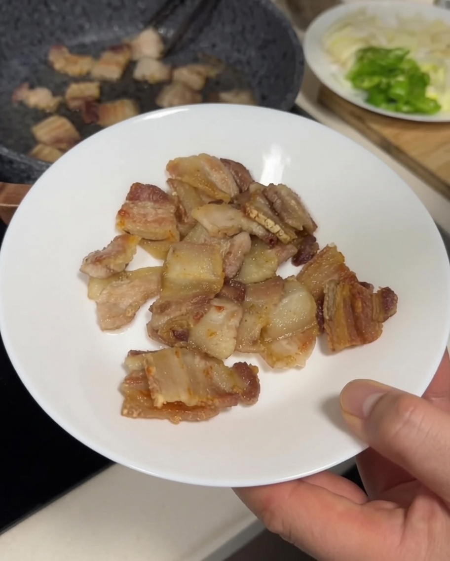 Goldbraune, knusprige Stücke Schweinebauch werden mit einer Zange auf einen weißen Teller gelegt.