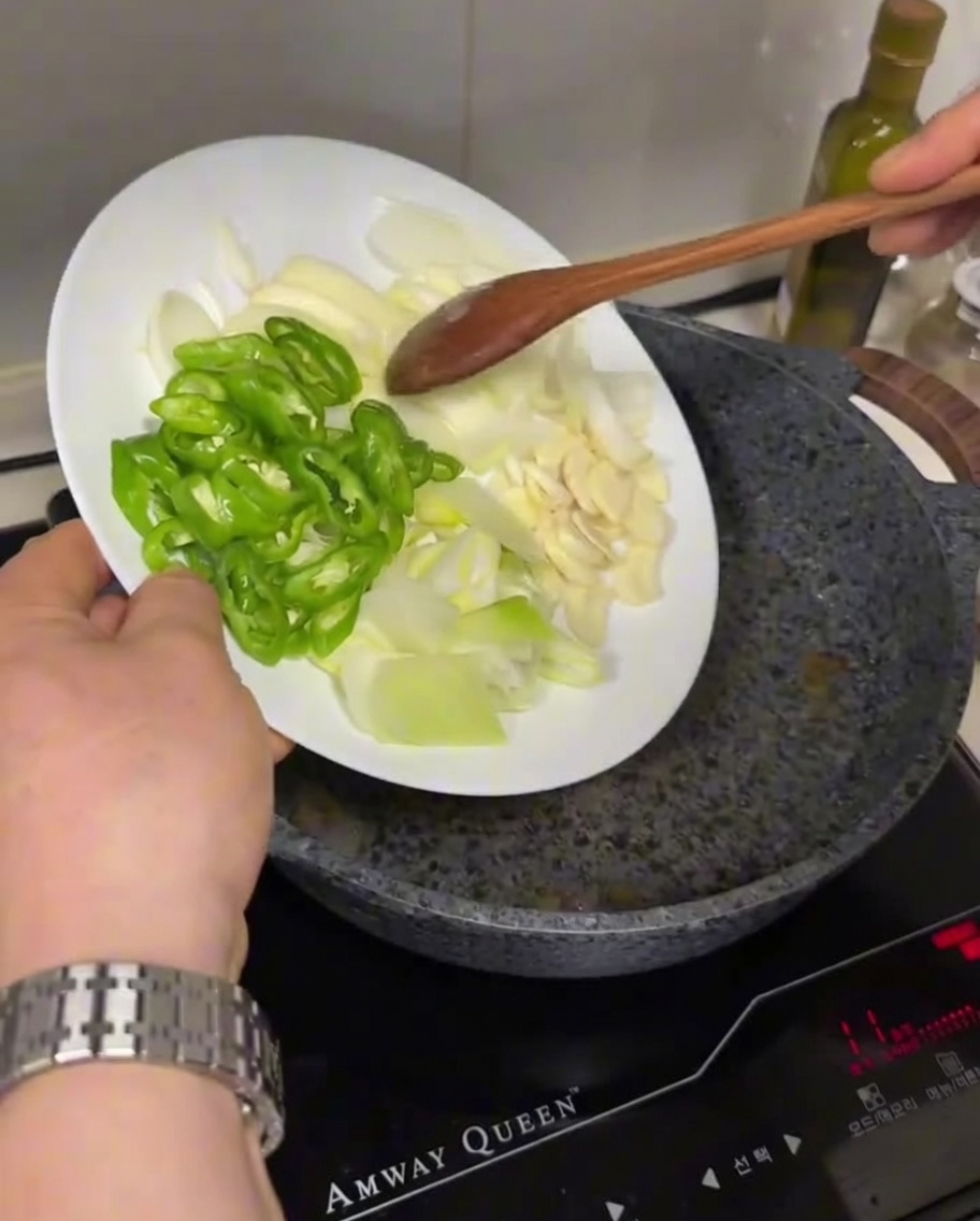 Geschnittene grüne Chilis, Zwiebeln und Knoblauch werden in eine heiße, geölte Pfanne gegeben.