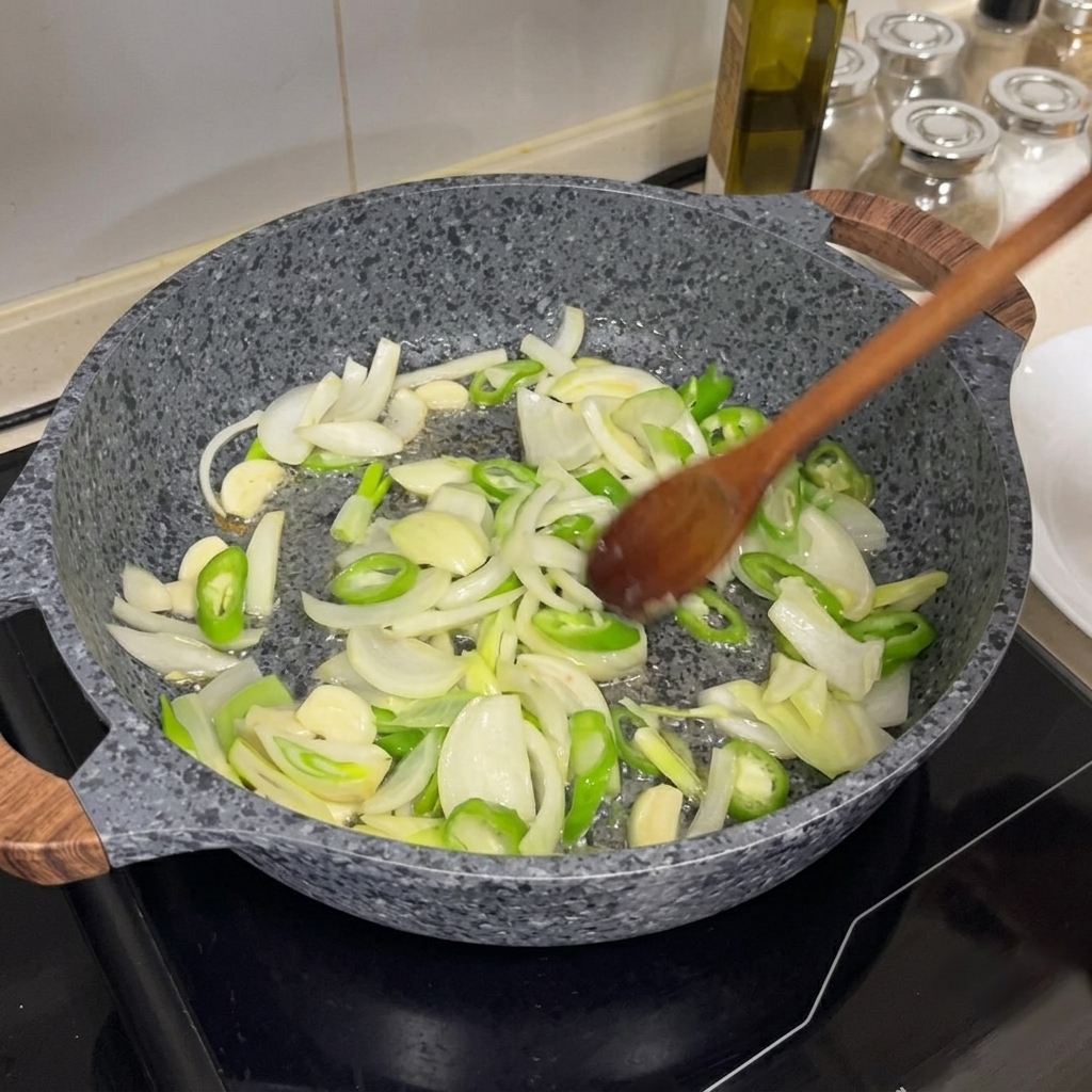 Zwiebeln, Chilis und Knoblauch werden in einer heißen Pfanne mit einem Holzlöffel angebraten.