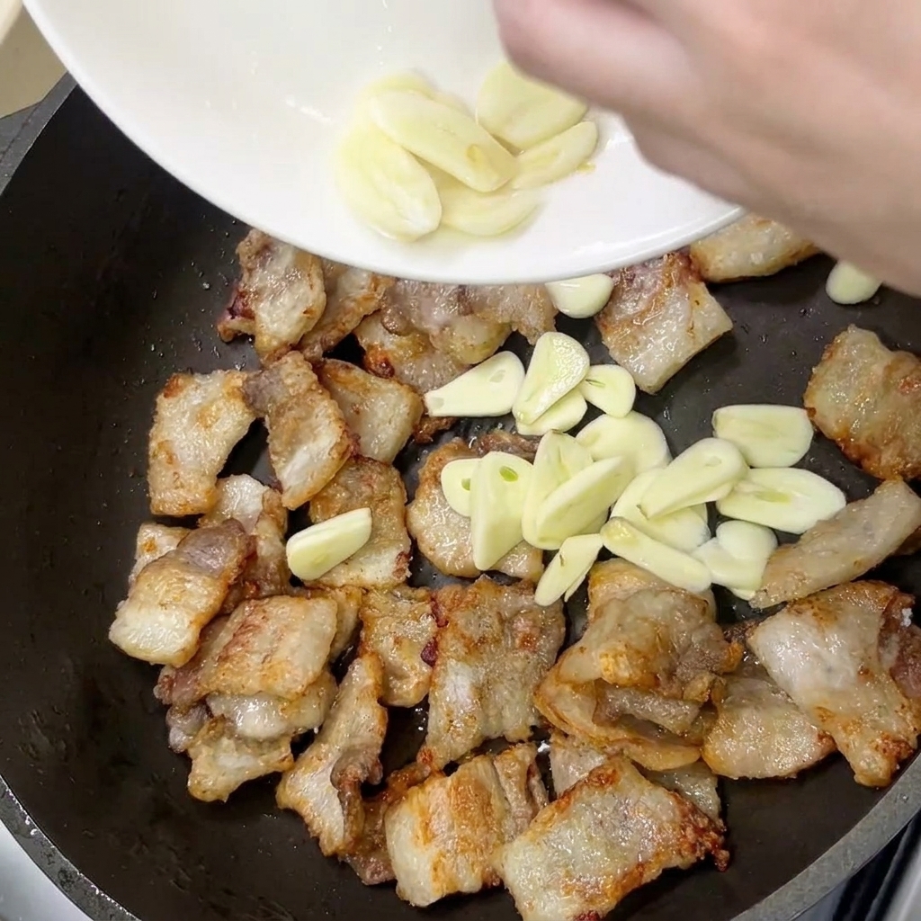 Frische Knoblauchscheiben werden in die Pfanne zum goldbraunen Schweinebauch gegeben.