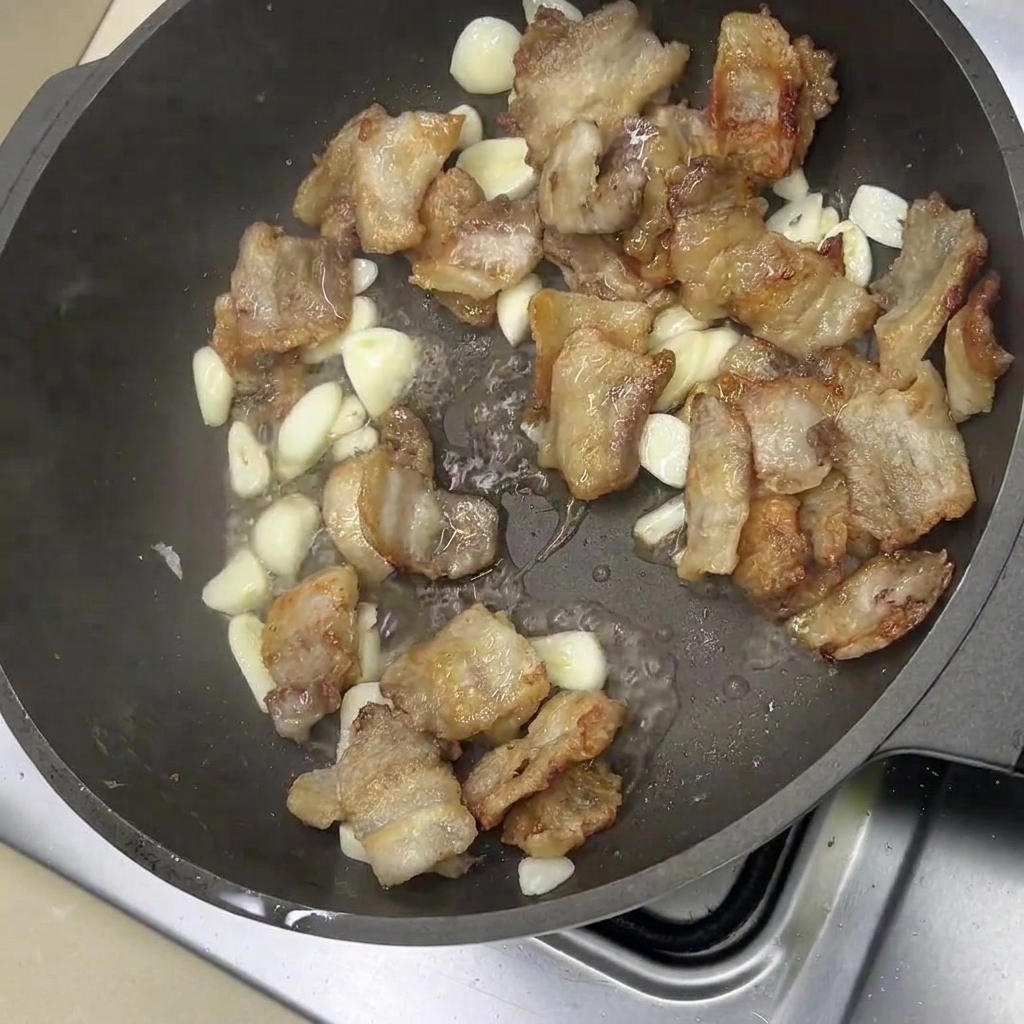 Gebratener Schweinebauch und Knoblauch brutzeln in einer Pfanne mit Gewürzen.