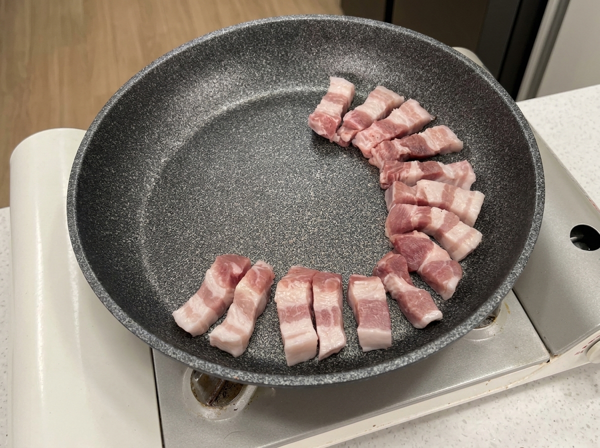 Rohe Schweinebauchscheiben in einer kreisförmigen Anordnung in einer grauen Antihaftpfanne.