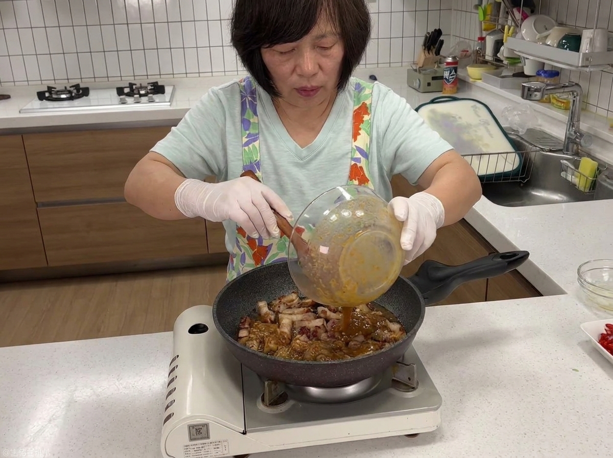 Dunkle Sojabohnenpasten-Sauce wird aus einer Schüssel in die Pfanne mit angebratenem Schweinefleisch gegossen.